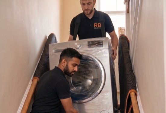 Two uniformed RB Removals team members safely carrying a heavy washing machine out of a residential property.