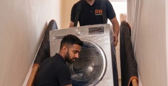 Two uniformed RB Removals team members safely carrying a heavy washing machine out of a residential property.