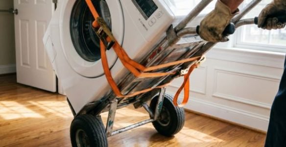 A heavy washing machine securely strapped to a professional appliance dolly for safe, damage-free transport.